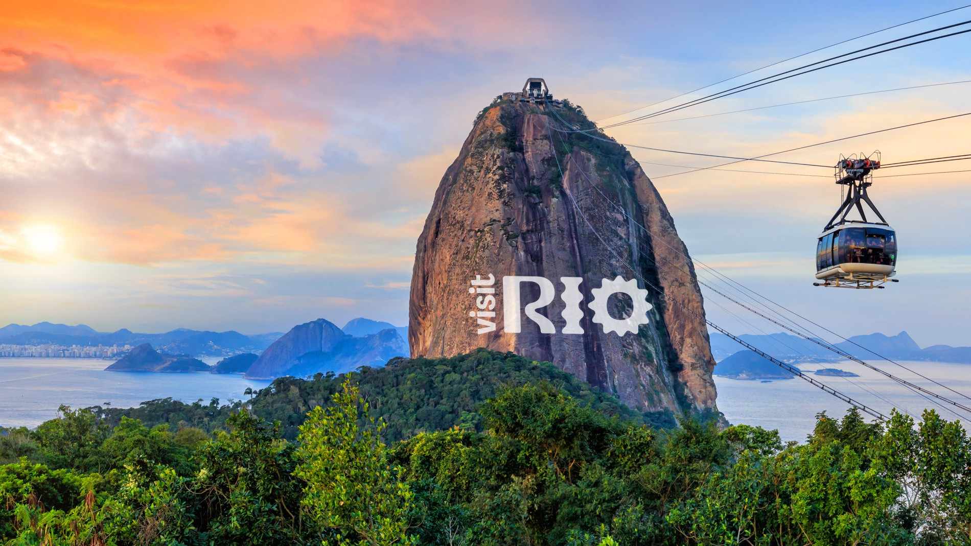 Sugarloaf Mountain and Guanabara Bay in Rio de Janeiro at first light, a cable car crossing between the peaks, with the “visit Rio” mark over the rock.