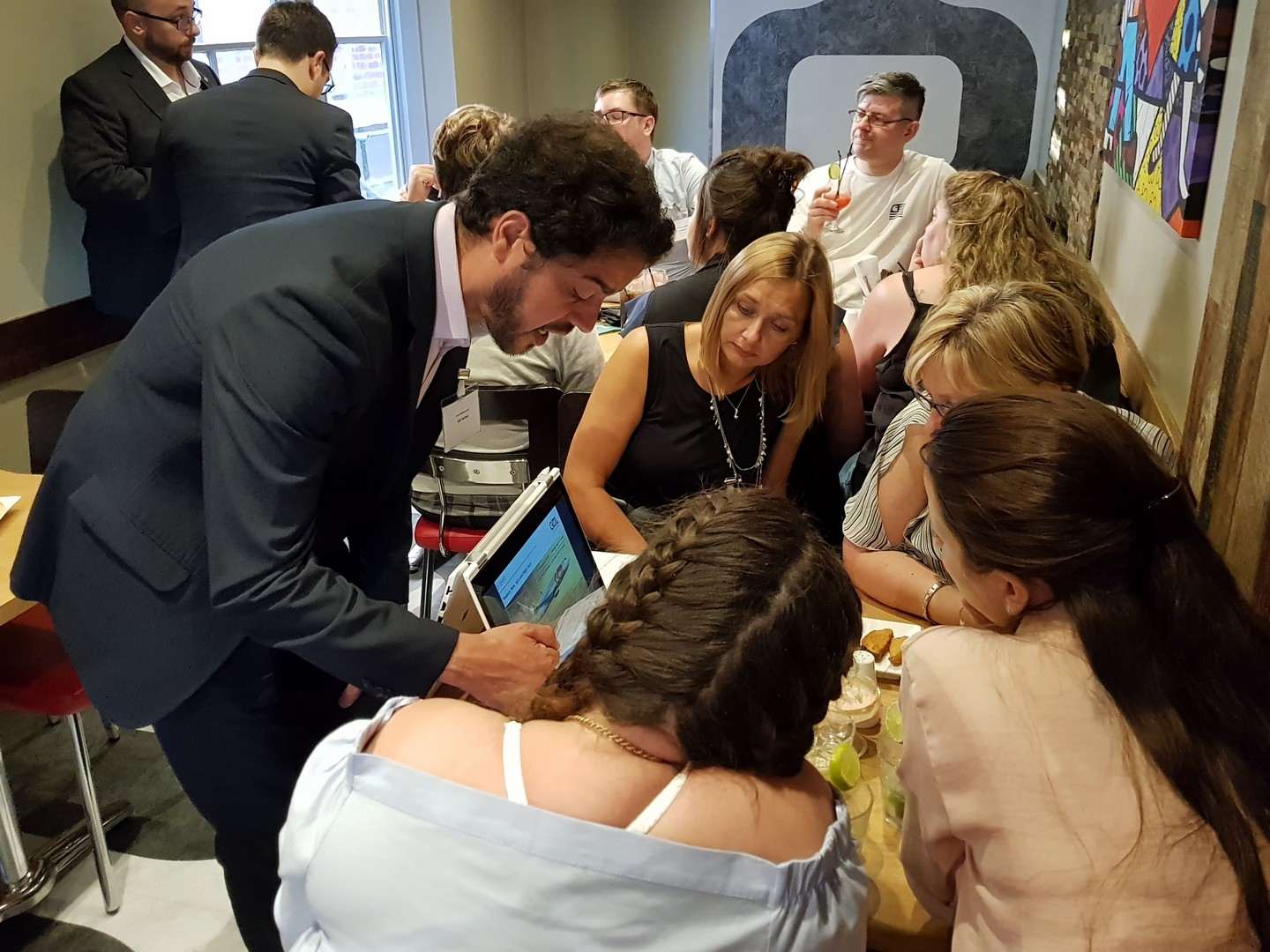 Travel trade professionals leaning in around a tablet during a Bossa roadshow.