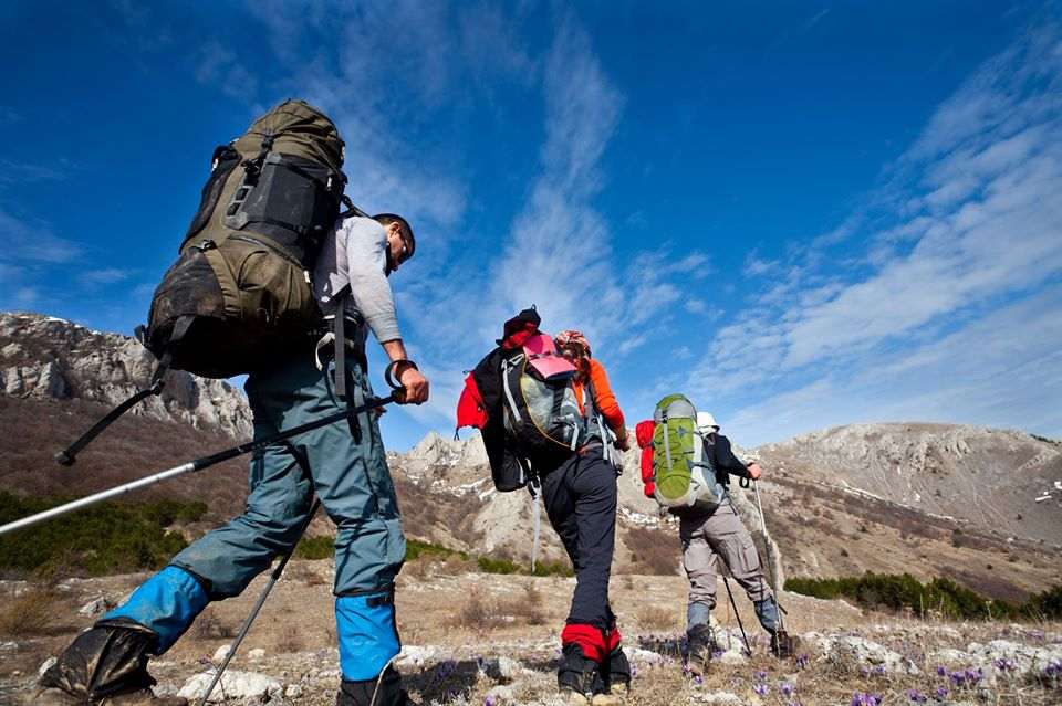 Hikers carrying full backpacks climbing a rocky ridge under a clear blue sky.